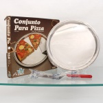 Conjunto para pizza confeccionado em aço inoxidável, marca Elmo Gazola, Brasil, século XX. Composto por prato circular de servir, com aba lisa e bordo moldado, acompanhado de utensílio para corte e serviço, dotado de lâmina serrilhada e cabo em material sintético vermelho. Conserva embalagem original com inscrições "Conjunto Para Pizza - Aço Inox", Elmo Gazela e "design 64". Embalagem com avarias, vide foto. Medidas: Comp.: 29 x Larg.: 5cm.Medida: Diam.: 31cm.