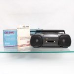 Rádio gravador estéreo CCE, modelo CS-2400, fabricado no Brasil. Aparelho portátil em gabinete de material sintético na tonalidade grafite, com alça articulada e antena telescópica. Reúne receptor analógico AM/FM estéreo e gravador/reprodutor de fitas cassete, dotado de sistema de parada automática (Automatic Stop System), controle de volume, sintonia, seleção de função, comandos de reprodução, gravação, avanço, retrocesso, pausa e parada/ejeção, além de entrada para fones de ouvido. Funcionamento elétrico, com alimentação pela rede ou por pilhas. Identificado no painel frontal como "CCE Stereo Radio Recorder CS-2400" e no reverso como produção da CCE da Amazônia S/A, Zona Franca de Manaus, indústria brasileira. Acompanha caixa original e manual de instruções/assistência técnica. Brasil, final do século XX. Funcionando. Medidas: Alt.: 18 x Comp.: 36 x Larg.: 9cm.