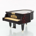 Caixa de música porta-joias em formato de piano de cauda, marca Kings; confeccionado em material sintético de tonalidade castanho-escura com decoração marmorizada avermelhada, teclado miniaturizado, pés com terminais dourados e pedais. Tampa articulada, com painel interno decorado por pautas musicais e figuras. Compartimento interno dividido, revestido em vermelho, com mecanismo musical incorporado. Placa frontal com inscrição "Kings". Medidas:
