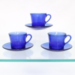 Três(03) xícaras para café com respectivos pires prensado translúcido de tonalidade azul cobalto, manufatura Duralex. Xícaras de bojo levemente obcônico, base circular espessa, bordo liso e asas curvas aplicadas; pires circulares de cavidade central demarcada e aba lisa. Conservam marca moldada "Duralex" e indicação de fabricação brasileira no fundo das xícaras. Medidas xícara: Alt.: 6,5 x Comp.: 10,5 x Larg.: 8 cm; Medida pires: Diam.: 13,5 cm.