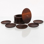 Conjunto de porta-copos com estojo em madeira nobre, comercializado por Azevedo Marques & Cia. Ltda., de estética modernista brasileira, circa 1950-60. O lote compreende um estojo cilíndrico com a inscrição dourada "Lembrança de Curitiba" na tampa, contendo seis porta-copos circulares em imbuia ou jacarandá com veios longitudinais aparentes. A base conserva etiqueta comercial em papel vermelho do estabelecimento na Rua Marechal Floriano, 243, em Curitiba, Paraná. Medidas caixa: Alt.: 4,5 x Diam.: 9,5cm; Medidas porta copos: Diam.: 6,5 cm.
