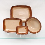 Três(03) travessas retangulares e um(01) bowl em cerâmica de grés de alta resistência, manufaturados pela oficina Oxford, fabricação nacional, c.1970-80. Apresentam esmaltagem vítrea acetinada com fundo em tom areia salpicado por minúsculas pontuações escuras, resultado da queima de minerais de ferro contidos na própria argila. A aba e fundo interno recebem decoração perimetral degradê em esmalte escorrido na cor castanha, resultando em transições lineares e nuances concêntricas diferenciadas para cada exemplar. A borda é rematada por filete liso de mesma tonalidade. O verso de cada peça exibe base com anel de assento aparente e carimbo de manufatura na cor azul sob o vidrado com as inscrições: "Grés / Oxford / Made in Brazil / 4830".  Medidas: Comp.: 16,5 x Larg.: 12,5cm; Comp.: 28 x Larg.: 21 cm; Comp.: 32 x Larg.: 26 cm; Medidas: Alt.: 7,5 x Diam.: 24 cm.