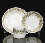 Porcelana Real, Mauá - SP(Fundada em 1943 por Fritz Erwin Schmidt). Trio para chá em porcelana nacional, c.1960/70. Composto de xícara para chá, pires e prato para sobremesa. Esmaltagem vítrea na cor branca, borda contornada por filete em prata, ornamentação perimetral contínua transferida sob o vidrado, composta por ramagens fitomórficas, folhas lanceoladas e corolas florais estilizadas em nuances de verde-oliva, ocre e castanho, com contornos lineares pretos e realces em esmalte branco, distribuídas no corpo da xícara e nas orlas do pires e do prato. Marca da manufatura no verso. Medida: Diam.: 23 cm. Medidas: Xícara: Alt.: 6 x Comp.: 11 x Larg.: 8 cm; Prato: Diam.: 19 cm; Pires: Diam.: 14 cm.