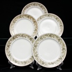 Conjunto composto por cinco(05) pratos rasos em porcelana nacional, c. 1960/70. Esmaltagem vítrea na cor branca, borda contornada por filete em prata, orla recebe ornamentação perimetral contínua transferida sob o vidrado, composta por ramagens fitomórficas, folhas lanceoladas e corolas florais estilizadas em nuances de verde-oliva, ocre e castanho, com contornos lineares pretos e realces em esmalte branco. Marca da manufatura no verso. Medida: Diam.: 25,5 cm.