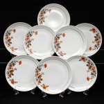 Porcelana Real, Mauá - SP(Fundada em 1943 por Fritz Erwin Schmidt). Conjunto de pratos para sobremesa em porcelana nacional, datável do período compreendido entre as décadas de 1950 e 1970. Esmaltagem vítrea na cor branca, aba delimitada por fino filete dourado aplicado sob a orla. A superfície recebe decoração assimétrica em decalcomania policroma, caracterizada por um ramo floral arqueado que se estende por dois terços da margem esquerda, composto por corolas em tonalidades rosa, ocre-alaranjado e cinza, guarnecidas por folhagens em tons terra, oliva e detalhes em hachuras escuras, além de pequenos cachos de bagas avermelhadas. Marca da manufatura no verso. Composto de oito(08) unidades. Medida: Diam.: 19 cm.