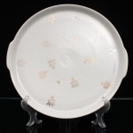 Porcelana Renner, Porto Alegre - RS (Fundada em 1937). Travessa circular em porcelana nacional, c.1960-70. Esmaltagem vítrea na cor branca, bordo elevado e duas pegas laterais integradas. Decoração composta por pequenos ramos florais em douradura distribuídos pelo campo. Apresenta leves desgastes na douradura. Marca no reverso: "Porcelana Renner - Porto Alegre". Medida: Diam.: 28 cm.