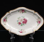 Porcellana Mauá, Mauá - SP(Fundada em 1937 por Fritz Erwin Schmidt / ativa até 1968). Travessa rasa em porcelana nacional, c.1940-50. Formato losangular com bordas arredondadas, levemente reviradas, e debrum recortado, delimitado por filete dourado aplicado na orla. Centro decorado por motivo pictórico decalcado composto por um buquê de rosas em tons de rubi, rosa-chá e branco, guarnecido por folhagens em verde-oliva e esmeralda, que se replicam  dispostos de forma simétrica nas quatro extremidades da aba. O reverso apresenta carimbo de manufatura, contendo a inscrição em arco "Porcellana Mauá" circundando o logotipo estilizado da empresa e a representação gráfica de uma locomotiva a vapor, em referência histórica à estrada de ferro regional. Medidas: Alt.: 3 x Comp.: 32,5 x Larg.: 22 cm.