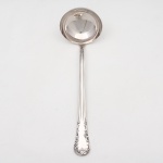 MERIDIONAL EPNS 100. Elegante concha para serviço confeccionada em metal espessurado à prata(EPNS 100), cabo violinado com filetes longitudinais em baixo-relevo e terminação ornamentada por composição de concheados, volutas, flores e folhagens em relevo. Marca da manufatura puncionada no verso. Medida: Comp.: 29 cm.