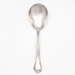 MERIDIONAL EPNS 100. Elegante colher para serviço confeccionada em metal espessurado à prata(EPNS 100), concha ligeiramente profunda de formato piriforme, cabo violinado com filetes longitudinais em baixo-relevo e terminação ornamentada por composição de concheados, volutas, flores e folhagens em relevo. Marca da manufatura puncionada no verso. Medida: Comp.: 21 x Larg.: 6 cm.