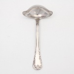 MERIDIONAL EPNS 100. Elegante concha para molho confeccionada em metal espessurado à prata(EPNS 100), bojo profundo de formato oblongo, dotado de vertedouros laterais e borda ondulada; cabo violinado com filetes longitudinais em baixo-relevo e terminação ornamentada por composição de concheados, volutas, flores e folhagens em relevo. Marca da manufatura puncionada no verso. Medida: Alt.: 14 x Comp.: 6,5 x Larg.: 4,5 cm.