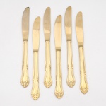 Belíssimo conjunto de facas confeccionadas em metal, dotado de profusa decoração em douradura, fabricação japonesa, manufatura For Ever; cabo de ponta oval, ornamentado por composição rocaille em relevo, constituída por volutas, concheados, flores e folhagens de inspiração Luís XV. Lâmina com dorso serrilhado. Marca da manufatura gravada na lâmina. Composto de seis(06) unidades. Medida: Comp.: 21,5 cm.