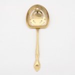 Belíssima colher para serviço(vegetais, guarnições ou frutas em calda) confeccionadas em metal, dotado de profusa decoração em douradura, fabricação japonesa, manufatura For Ever; lâmina ligeiramente profunda, vazada, com formato arredondado, cabo de ponta oval, ornamentado por composição rocaille em relevo, constituída por volutas, concheados, flores e folhagens de inspiração Luís XV. Marca da manufatura no verso do cabo. Medida: Comp.: 22 cm.