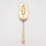 Belíssima espátula para servir torta(pie/cake server) confeccionada em metal, dotado de profusa decoração em douradura, fabricação japonesa, manufatura For Ever; lâmina ligeiramente profunda, vazada, com formato arredondado, cabo de ponta oval, ornamentado por composição rocaille em relevo, constituída por volutas, concheados, flores e folhagens de inspiração Luís XV. Marca da manufatura no verso do cabo. Medida: Comp.: 27 cm.