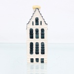 Garrafa miniatura em porcelana moldada em forma de casa holandesa, pertencente à série de casas Delft produzidas para a KLM (Koninklijke Luchtvaart Maatschappij, companhia aérea neerlandesa fundada em 1919) e destinada ao acondicionamento de Bols Genever(destilado tradicional neerlandês à base de grãos e aromatizado com zimbro, produzido pela casa Lucas Bols, fundada em Amsterdã em 1575). Corpo arquitetônico de planta retangular, com fachadas moldadas em relevo simulando alvenaria, portas e janelas, cobertura inclinada com telhas em relevo, águas-furtadas e chaminé utilizada como gargalo, fechada por tampa. Esmaltação vítrea em branco, azul-escuro e azul acinzentado. Verso com as inscrições 64, Bols Amsterdam 1575 e logotipo KLM. Base com as inscrições 52, Bols Amsterdam 1575 e logotipo KLM. Base com inscrição Blue Delfts exclusively made for KLM by Bols Amsterdam 1575, código HKDNP e numeração moldada 2012 52. KLM House nº 52. Medidas: Alt.: 11,5 x Comp.: 4 x Larg.: 4,5cm.