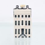 Garrafa miniatura em porcelana moldada em forma de casa holandesa, pertencente à série de casas Delft produzidas para a KLM (Koninklijke Luchtvaart Maatschappij, companhia aérea neerlandesa fundada em 1919) e destinada ao acondicionamento de Bols Genever(destilado tradicional neerlandês à base de grãos e aromatizado com zimbro, produzido pela casa Lucas Bols, fundada em Amsterdã em 1575). Corpo arquitetônico de planta retangular, com fachadas moldadas em relevo simulando alvenaria, portas e janelas, cobertura inclinada com telhas em relevo e chaminé utilizada como gargalo, fechada por tampa. Esmaltação vítrea em branco, azul-escuro e azul acinzentado. Verso com a númeração 83 sobre as inscrições Bols Amsterdam 1575 e logotipo KLM. Base com inscrição "Blue Delfts exclusively made for KLM by Bols Amsterdam 1575 " e numeração em baixo-relevo "2011 - 83". Medidas: Alt.: 10 x Comp.: 5,5 x Larg.: 4,5cm. (Esta 83ª casa da série KLM está localizada no número 672 da Keizersgracht, em Amsterdã, e foi construída em 1671).