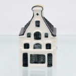 Garrafa miniatura em porcelana moldada em forma de casa holandesa, pertencente à série de casas Delft produzidas para a KLM (Koninklijke Luchtvaart Maatschappij, companhia aérea neerlandesa fundada em 1919) e destinada ao acondicionamento de Bols Genever(destilado tradicional neerlandês à base de grãos e aromatizado com zimbro, produzido pela casa Lucas Bols, fundada em Amsterdã em 1575). Corpo arquitetônico de planta retangular, com fachadas moldadas em relevo simulando alvenaria, portas e janelas, cobertura inclinada com telhas em relevo e chaminé utilizada como gargalo, fechada por tampa. Esmaltação vítrea em branco, azul-escuro e azul acinzentado. Verso com a númeração 66 sobre as inscrições Bols Amsterdam 1575 e logotipo KLM. Base com inscrição "Blue Delfts exclusively made for KLM by Bols Amsterdam 1575 ", "Bols Genever 35ML" e numeração em baixo-relevo "2022 - 66". Medidas: Alt.: 9,5 x Comp.: 5,5 x Larg.: 5,5cm. (Esta 66ª casa da série KLM está localizada no número 403 da Keizersgracht , Amsterdã, foi construída em 1669 e reconstruída em 1949).