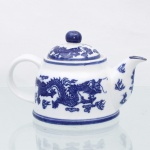 Bule para chá em porcelana chinesa, de bojo globular achatado, com alça arqueada, bico vertedor curvo e tampa de encaixe com pomo esférico. Esmaltação vítrea na cor branca, com decoração em azul sob o vidrado composta por dragões chineses de cinco garras entre nuvens estilizadas e chamas, distribuídos ao redor do bojo; tampa com motivos de dragões e nuvens. Filetes azuis circundam a base, o bordo, a tampa e o bico vertedor. Base com marca Happy Dining-Room / Microwave Oven Safe / Made in China / 1999 (K-44), indicando fabricação chinesa contemporânea, datada de 1999. Medidas: Alt.: 10,5 x Comp.: 18 x Larg.: 11,5cm.