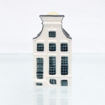 Garrafa miniatura em porcelana moldada em forma de casa holandesa, pertencente à série de casas Delft produzidas para a KLM (Koninklijke Luchtvaart Maatschappij, companhia aérea neerlandesa fundada em 1919) e destinada ao acondicionamento de Bols Genever(destilado tradicional neerlandês à base de grãos e aromatizado com zimbro, produzido pela casa Lucas Bols, fundada em Amsterdã em 1575). Corpo arquitetônico de planta retangular, com fachadas moldadas em relevo simulando alvenaria, portas e janelas, cobertura inclinada com telhas em relevo e chaminé utilizada como gargalo, fechada por tampa. Esmaltação vítrea em branco, azul-escuro e azul acinzentado. Verso com a númeração 63 sobre as inscrições Bols Amsterdam 1575 e logotipo KLM. Base com inscrição "Blue Delfts exclusively made for KLM by Bols Amsterdam 1575 - Bols Genever 35 ml" e numeração moldada "2023 - 63". Medidas: Alt.: 10 x Comp.: 5,5 x Larg.: 5,5cm.