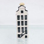 Garrafa miniatura em porcelana moldada em forma de casa holandesa, pertencente à série de casas Delft produzidas para a KLM (Koninklijke Luchtvaart Maatschappij, companhia aérea neerlandesa fundada em 1919) e destinada ao acondicionamento de Bols Genever(destilado tradicional neerlandês à base de grãos e aromatizado com zimbro, produzido pela casa Lucas Bols, fundada em Amsterdã em 1575). Corpo arquitetônico de planta retangular, com fachadas moldadas em relevo simulando alvenaria, portas e janelas, cobertura inclinada com telhas em relevo e chaminé utilizada como gargalo, fechada por tampa. Esmaltação vítrea em branco, azul-escuro e azul acinzentado. Casa de canal número 46. Base contendo as inscrições: "Blue Delfts exclusively made for KLM by Bols - Amsterdam 1575", "HKDNP" e e numeração em baixo-relevo "2012 - 46". Medidas: Alt.: 11,5 x Comp.: 4 x Larg.: 5cm.
