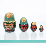 Conjunto de bonecas tradicionais russas do tipo matryoshka, confeccionado em madeira torneada e pintada à mão. Composto por quatro figuras encaixáveis de dimensões decrescentes, o grupo apresenta acabamento em verniz sobre fundo dividido entre tonalidades verde-esmeralda na porção superior e preto na base. A ornamentação exibe feições estilizadascom cabelos avermelhados sob lenço de cabeça (shashura) pontuado por motivos circulares, seguidos por uma barra festonada em tom ocre. O ventre de cada figura abriga composição pictórica policromada com arranjos de bagas avermelhadas e folhagens verdes estilizadas, ladeados por pequenos grupos de sementes pontilhadas. Medidas: Alt.: 7,5 x Diam.: 5cm.Medidas: Alt.: 5,5 x Diam.: 3,5cm.Medidas: Alt.: 4 x Diam.: 2,5cm.Medidas: Alt.: 2,5 x Diam.: 1,5cm.