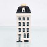 Garrafa miniatura em porcelana moldada em forma de casa holandesa, pertencente à série de casas Delft produzidas para a KLM (Koninklijke Luchtvaart Maatschappij, companhia aérea neerlandesa fundada em 1919) e destinada ao acondicionamento de Bols Genever(destilado tradicional neerlandês à base de grãos e aromatizado com zimbro, produzido pela casa Lucas Bols, fundada em Amsterdã em 1575). Corpo arquitetônico de planta retangular, com fachadas moldadas em relevo simulando alvenaria, portas e janelas, cobertura inclinada com telhas em relevo e chaminé utilizada como gargalo, fechada por tampa. Esmaltação vítrea em branco, azul-escuro e azul acinzentado. Verso com a númeração 74 sobre as inscrições Bols Amsterdam 1575 e logotipo KLM. Base com inscrição "Blue Delfts exclusively made for KLM by Bols Amsterdam 1575 ", "HKDNP" e numeração em baixo-relevo "2012 - 84". Medidas: Alt.: 10,5 x Comp.: 4,5 x Larg.: 4,5cm. (Esta 74ª casa da série KLM está localizada no número 7 da Reguliersgracht, em Amsterdã, Construído no século XVII e reconstruída diversas vezes).