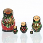 Conjunto de bonecas tradicionais russas do tipo matryoshka, confeccionado em madeira torneada e pintada à mão. Composto por cinco figuras encaixáveis de dimensões decrescentes, o grupo apresenta acabamento em verniz sobre fundo dividido entre tonalidades pretas na porção superior e vermelhas na base da saia, delimitada por contorno festonado claro. A decoração exibe feições femininas estilizadas com cabelos castanhos sob lenço de cabeça (shashura) decorado por debrum dourado e pontilhados abstratos. O ventre das figuras principais abriga composição pictórica de inspiração Khokhloma, contendo arranjo de pequenas bagas vermelhas com miolos claros, folhas lanceoladas verdes e gavinhas em ouro fosco, motivo decorativo que se estende de forma simplificada para o reverso do lenço e para as peças menores. Medidas: Alt.: 8 x Diam.: 4,5cm.Medidas: Alt.: 5,5 x Diam.: 3cm.Medidas: Alt.: 4 x Diam.: 2,5cm.Medidas: Alt.: 3 x Diam.: 1,5cm.Medidas: Alt.: 1,5 x Diam.: 1cm.