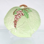 Travessa executada em faiança inglesa, manufatura Carlton Ware. Corpo moldado em formato de folha(saladware), com nervuras e reticulação vegetal em relevo, esmaltado em tonalidade verde-clara. Decoração policroma aplicada em relevo representando ramo de dedaleira (Digitalis), com inflorescências pendentes em tons rosados e folhagem verde, complementada por haste arqueada formando pega na parte superior. Reverso esmaltado em branco, com marca de fábrica "Carlton Ware  Made in England  Trade Mark Registered" e inscrição "Australian Design  Registration Applied For", referente ao registro do desenho destinado ao mercado australiano. Manufatura Carlton Ware, Stoke-on-Trent, Inglaterra. Medidas: Comp.: 18 x Larg.: 16,5cm.