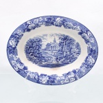Wood & Sons, Burslem - Inglaterra(Fundada em 1865). Excepcional travessa funda de formato oval em faiança inglesa da década de 1920. Esmaltagem vítrea na cor branca, profusa decoração por transferência em azul sob o vidrado, intitulada Enoch Woods English Scenery", apresentando paisagem rural inglesa com arquitetura campestre, igreja, arvoredo, curso dágua, personagens e rebanho. Aba ornamentada por friso contínuo de flores, folhagens e ramagens sobre fundo azul pontilhado. Borda contornada por friso de tonalidade azul cobalto. No verso, marca de fábrica "Enoch Woods English Scenery  Woods Ware  Wood & Sons  England". Medidas: Alt.: 5 x Comp.: 26,5 x Larg.: 20,5 cm.