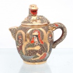 Bule em faiança japonesa Satsuma - Japão, período Meiji ao Taish, circa 1900-1920. Corpo globular com tampa, bico curto e alça lateral; tampa encimada por pomo escultórico em forma de dragão, com cabeça e boca aberta. Apresenta cobertura em esmalte em tonalidade castanho-avermelhada, extensa douradura e ornamentação em esmaltes policromos espessos em relevo pela técnica moriage. A iconografia central retrata a deidade budista Kannon(Avalokiteshvara) entronizada, circundada pelas figuras de quatro Arhats(Rakan), imersos em halos circulares dourados com grafismos geométricos. Alça, bico e tampa recebem ornamentação pontilhista em esmalte branco, vermelho e dourado, complementada por padrões geométricos. Na base, ostenta marcação heráldica da família Shimazu - cruz inscrita em círculo - e assinatura em pigmento vermelho-ferro, com os caracteres kanji atribuídos a Okura / Ogura Renzan. Apresenta craquelado característico do material e do período. Medidas: Alt.: 13,5 x Comp.: 14 x Larg.: 9cm.