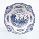 Johnson Brothers, Hanley Inglaterra(fundada em 1883 pelos irmãos Alfred, Frederick e Henry Johnson). Belíssimo bowl em faiança inglesa, c1930/40, pertencente à série "Old Britain Castles". Esmaltagem vítrea de tom marfim claro, formato hemisférico, aba modelada com ligeira ondulação e orla guarnecida por cercadura geométrica contínua na cor azul. A superfície recebe ornamentação de transferência sob o vidrado em tom azul-cobalto, baseada nas matrizes gravadas em 1928 por Miss Fennel, composta por cartelas festonadas com motivos de treliças, volutas acantiformes e buquês florais. Centro abriga composição pictórica que reproduz uma gravação manual, retratando o monumento fortificado de Ruthin Castle situado no País de Gales, com a inscrição inferior "Ruthin Castle in 1792", detalhando a estrutura acastelada, torres e figuras humanas passantes em estrada arborizada sob céu nublado delineado em hachuras. Verso exibe base com anel de assento aparente e carimbo de manufatura transferido na cor azul, composto por uma coroa imperial encimando as inscrições "Johnson Bros - Made in England - Old Britain Castles". Medidas: Alt.: 6 x Diam.: 21 cm.