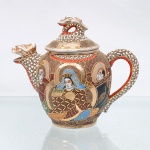 Bule em porcelana japonesa executado ao estilo Satsuma. Corpo globular com tampa, bico e alça de conformação zoomórfica, ambos terminados em cabeças de dragão, e pomo da tampa igualmente modelado como dragão. Apresenta cobertura integral em esmalte marfim translúcido com craquelê , ornamentação pictórica em esmaltes policromos e elementos em relevo pela técnica moriage, associados a extensas áreas de douradura. A iconografia central retrata a deidade budista Kannon(Avalokiteshvara) entronizada, circundada pelas figuras de quatro Arhats(Rakan), imersos em halos circulares dourados com grafismos geométricos. Dragões percorrem o corpo, a alça e a tampa, com escamas pontilhadas em esmalte branco, contornos dourados e detalhes em vermelho. Ausência de marca de manufatura. Medidas: Alt.: 14,5 x Comp.: 17 x Larg.: 9 cm.