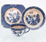 Trio para chá em faiança japonesa, Imperial Ironstone Ware, N.K.T., Japão, meados do século XX. Composto por xícara, pires e prato de sobremesa quadrangular com cantos arredondados. Decoração derivada do Willow Pattern, em azul sob esmalte, com paisagem orientalista constituída por arquitetura, ponte, arvoredo, curso d'água, embarcação e aves em voo; cercaduras geométricas em azul e sépia e filetação dourada. Superfície com craquelê de esmalte. No reverso, marca "Imperial Ironstone Ware - N.K.T. - Made in Japan", vinculada à produção da Nihon Koshitsu Toki, atual NIKKO, manufatura fundada em Kanazawa em 1908. Medidas xícara: Alt.: 5,5 x Comp.: 10 x Larg.: 8cm.Medidas pires: Diam.: 13,5cm.Medidas prato: Comp.: 14 x Larg.: 14cm.