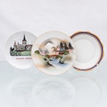Três(03) pratos decorativos em porcelana de diferentes manufaturas, datáveis da segunda metade do século XX. O primeiro exemplar, de formato circular regular em porcelana branca vidrada, apresenta decoração policroma de caráter turístico retratando a silhueta arquitetônica da zona histórica de Tallinn com a legenda "TALLINN ESTONIA", exibindo no reverso a marca da fábrica polonesa Lubiana acompanhada pelo carimbo oficinal "KÄSITÖÖ TÜ HOP H. PALJAK". O segundo constitui um prato de sobremesa em porcelana casca de ovo japonesa de exportação, ostentando em todo o centro pintura manual de paisagem tradicional nipônica com pagode, ponte arqueada (taikobashi) em tom terracota e o Monte Fuji ao fundo sob névoa ocre, trazendo no reverso a marca geométrica losangular impressa em pigmento coral com os dizeres 'MADE IN JAPAN". O terceiro item configura um prato de sobremesa em porcelana fina da manufatura brasileira Porcelana Renner, produzida em Porto Alegre, Rio Grande do Sul, com aba recortada em formato sextavado sutil e debrum ondulado em ouro, guarnecido por proeminente cercadura azul-cobalto decorada com volutas, palmetas e motivos geométricos neoclássicos aplicados em douramento; o reverso ostenta o carimbo oficinal verde sob o vidrado com o nome da empresa ladeado por estrelas e a indicação de procedência. Medidas: Diam.: 16,5 cm; Diam.: 17,5 cm; Diam: 19 cm.