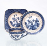Trio para chá em faiança japonesa, Imperial Ironstone Ware, N.K.T., Japão, meados do século XX. Composto por xícara, pires e prato de sobremesa quadrangular com cantos arredondados. Decoração derivada do Willow Pattern, em azul sob esmalte, com paisagem orientalista constituída por arquitetura, ponte, arvoredo, curso d'água, embarcação e aves em voo; cercaduras geométricas em azul e sépia e filetação dourada. Superfície com craquelê de esmalte. No reverso, marca "Imperial Ironstone Ware - N.K.T. - Made in Japan", vinculada à produção da Nihon Koshitsu Toki, atual NIKKO, manufatura fundada em Kanazawa em 1908. Medidas xícara: Alt.: 5,5 x Comp.: 10 x Larg.: 8cm.Medidas pires: Diam.: 13,5cm.Medidas prato: Comp.: 14 x Larg.: 14cm.