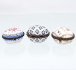 Três(03) caixas porta-joias em porcelana, coleção Porcelain Art. Caixas de formato oval, destinadas à guarda de anéis, brincos e pequenos objetos de adorno pessoal, com tampas abauladas articuladas por dobradiças, guarnições metálicas ornamentadas e fechos frontais. Decoração policromada realçado com douradura, compreendendo motivos florais, frisos estilizados e composição geométrica reticulada em azul e ouro. Uma das peças apresenta no reverso marca estampada "Porcelain Art  PA". Medidas: Alt.: 4 x Comp.: 5 x Larg.: 4,5cm.