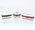 Três(03) caixas porta-joias em porcelana, coleção Porcelain Art. Caixas de pequenas dimensões, em formatos retangular, oval e oblongo, destinadas à guarda de anéis, brincos e outros objetos de adorno pessoal. Apresentam tampas articuladas por dobradiças, guarnições metálicas ornamentadas e fechos frontais. Decoração policromada com motivos florais, festões, frisos geométricos e elementos em douradura, em diferentes composições. Duas peças apresentam no reverso marca estampada "Porcelain Art - PA". Medidas: Alt.: 3 x Comp.: 7,5 x Larg.: 3,5cm; Medidas: Alt.: 3,5 x Comp.: 4,5 x Larg.: 4cm.