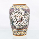 Vaso executado em faiança portuguesa, produzido pelo Atelier B.L., Condeixa-a-Velha, região de Coimbra, Portugal. Corpo ovóide, colo curto e boca circular, integralmente decorado à mão segundo repertório inspirado na cerâmica portuguesa dos séculos XVII e XVIII, tradição característica da produção de Condeixa. Composição organizada em reservas de contorno recortado, preenchidas por lebres, elementos florais, ramagens, frutos e motivos vegetalistas, intercaladas por campos reticulados. Faixas de enrolamentos de acanto delimitam o ombro e a seção inferior, em policromia de azul, amarelo, verde, vermelho, castanho e negro. Base marcada "228 / Atelier B.L. / Coimbra / Portugal / Séc. XVII", inscrição que indica a referência histórica do padrão decorativo, e não a data de fabricação da peça. O Atelier B.L., identificado pela Câmara Municipal de Condeixa como oficina de Belmiro Miranda Quitério, integra a produção cerâmica de Condeixa-a-Velha. A própria municipalidade registra que essa tradição emprega pintura inspirada na cerâmica portuguesa dos séculos XVII e XVIII. Medidas: Alt.: 21,5 x Diam.: 13cm.