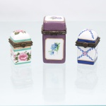 Três(03) caixas porta-joias em porcelana, coleção Porcelain Art, século XX. Caixas de formato quadrangular e alturas distintas, destinadas à guarda de joias e pequenos objetos pessoais, com tampas articuladas, montagens metálicas ornamentadas e fechos frontais. Decoração policromada variada: uma com motivos florais em rosa e verde; outra com fundo lilás e reservas delimitadas por filetes dourados contendo ramos florais; e a terceira com composição geométrica em azul-cobalto, vermelho e dourado. Bases com marca estampada "Porcelain Art - PA". Medidas: Alt.: 5,5 x Comp.: 3 x Larg.: 4cm.Medidas: Alt.: 4 x Comp.: 2,5 x Larg.: 3,5cm.