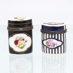 Duas(02) caixas porta-joias em porcelana, colelção Porcelain Art. Caixas de formato retangular vertical, destinadas à guarda de pequenas joias e objetos pessoais, com tampas articuladas, montagens metálicas e fechos frontais. Uma apresenta fundo preto com reservas de contorno recortado contendo buquês de rosas policromadas, delimitadas por filetes dourados; a outra, composição de faixas verticais em azul-cobalto, branco e dourado, intercaladas por reservas florais. Tampas com decoração correspondente. Apresentam marca na base "Porcelain Art  PA". Medidas: Alt.: 6 x Comp.: 4 x Larg.: 4cm.Medidas: Alt.: 5 x Comp.: 4,5 x Larg.: 3,5cm.