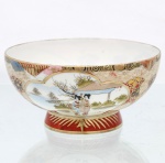 Bowl sobre pedestal em porcelana dita "casca de ovo", manufaturada no Japão durante o período Taisho ou início da era Showa, correspondente à primeira metade do século XX, destinada ao mercado de exportação ocidental. A peça apresenta formato hemiesférico assentado sobre pé circular elevado, ornado na base por faixa em tom vermelho-ferro guarnecida por motivos radiantes estilizados em ouro. O corpo externo exibe fundo densamente decorado com padrões geométricos e florais tradicionais, incluindo reticulados, espirais karakusa e painéis em forma de leque, que emolduram duas grandes cartelas polilobadas opostas. A primeira reserva abriga pintura manual policroma com representação narrativa de duas figuras femininas (geishas ou bijin) trajando quimonos formais em meio a uma paisagem ajardinada com pavilhão arquitetônico e pinheiros. A segunda cartela delimita cena de cariz topográfico composta por cabana rural ladeada por coníferas, margem lacustre e montanhas delineadas sob névoa ao fundo. Borda superior recebe filete dourado sobre cercadura contínua preta e vermelha. Apresenta marca de manufatura ao fundo, praticamente ilegível. Possui fios de cabelo, visíveis nas fotografias. Medidas: Alt.: x Diam.: 7,5 x Diam.: 15,5 cm.