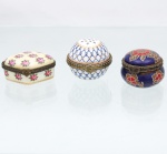 Três(03) caixas porta-joias em porcelana, coleção Porcelain Art, século XX. Caixas de pequenas dimensões, destinadas à guarda de joias e objetos pessoais, com tampas articuladas, aros metálicos e fechos frontais. Compreende exemplar retangular de fundo marfim decorado com rosas; peça esférica com reticulado azul-cobalto, ornatos dourados e fecho em forma de flor; e caixa circular de fundo azul-cobalto com motivos florais estilizados em vermelho, castanho e branco.Apresentam na base marca "Porcelain Art  PA".Medidas: Alt.: 2,5 x Comp.: 5,5 x Larg.: 4,5cm.Medidas: Alt.: 3 x Diam.: 4cm.Medidas: Alt.: 4 x Diam.: 4cm.