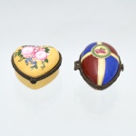Duas(02) caixas porta-joias em porcelana, coleção Porcelain Art. Peças destinadas à guarda de joias e pequenos objetos pessoais, com tampas articuladas, montagens metálicas e fechos frontais. Uma em formato de coração, com fundo amarelo e decoração floral policroma de rosas e pequenas flores azuis; outra de formato ovoide, decorada em campos alternados azul-cobalto e bordô, separados por faixas em tom creme e filetes dourados, com medalhão floral no topo. Apresentam na base a marca "Porcelain Art - PA".Medidas: Alt.: 4 x Comp.: 6,5 x Larg.: 5,5cm.Medidas: Alt.: 3,5 x Comp.: 5,5 x Larg.: 5,5cm.