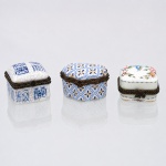 Três(03) caixas porta-joias em porcelana, coleção Porcelain Art. Caixas de pequenas dimensões, destinadas à guarda de joias e pequenos objetos pessoais, com corpos de contornos distintos, tampas abauladas articuladas por dobradiças, aros metálicos e fechos frontais. A primeira apresenta decoração em azul sob esmalte, com craquelado generalizado; a segunda, ornamentação geométrica seriada em azul e amarelo; a terceira, fundo branco com reservas florais policromas e frisos lineares. Apresentam na base a marca "Porcelain Art - PA". Medidas: Alt.: 3,5 x Comp.: 4 x Larg.: 4,5cm.Medidas: Alt.: 3,5 x Comp.: 5 x Larg.: 5cm.Medidas: Alt.: 3 x Comp.: 4 x Larg.: 5cm.