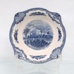 Johnson Brothers, Hanley Inglaterra(fundada em 1883 pelos irmãos Alfred, Frederick e Henry Johnson). Belíssimo bowl em faiança inglesa, c1930/40, pertencente à série "Old Britain Castles". Esmaltagem vítrea de tom marfim claro, formato hemisférico, aba modelada com ligeira ondulação e orla guarnecida por cercadura geométrica contínua na cor azul. A superfície recebe ornamentação de transferência sob o vidrado em tom azul-cobalto, baseada nas matrizes gravadas em 1928 por Miss Fennel, composta por cartelas festonadas com motivos de treliças, volutas acantiformes e buquês florais. Centro abriga composição pictórica que reproduz uma gravação manual, retratando o monumento fortificado de Bolsover Castle situado em Derbyshire, Inglaterra, com a inscrição inferior "Bolsover Castle in 1792", detalhando a torre de menagem, muralhas ameadas e colinas arborizadas delineadas em hachuras. Verso exibe base com anel de assento aparente e carimbo de manufatura transferido na cor azul, composto por uma coroa imperial encimando as inscrições "Johnson Bros - Made in England - Old Britain Castles". Medidas: Alt.: 7,5 x Diam.: 28 cm.