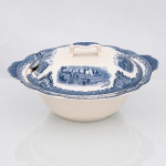Johnson Brothers, Hanley Inglaterra (fundada em 1883 pelos irmãos Alfred, Frederick e Henry Johnson). Belíssima terrina coberta, para legumes, em faiança inglesa, c1930/40, pertencente à série "Old Britain Castles", manufaturada pela oficina Johnson Brothers em Staffordshire, Inglaterra, pertencente à série "Old Britain Castles" de meados do século XX, circa 1930-1960. Esmaltagem vítrea na cor marfim, bojo hemisférico dotado de duas abas laterais salientes integradas, bordas recortadas em gomos ondulares e orla guarnecida por cercadura geométrica contínua na cor azul. A superfície externa e o topo da tampa recebem ornamentação de transferência sob o vidrado em tom azul-cobalto, baseada nas matrizes gravadas em 1928 por Miss Fennel, composta por cartelas festonadas com motivos de treliças, volutas acantiformes e buquês florais, e composição pictórica que reproduz uma gravação manual, retratando o monumento fortificado de Bolsover Castle com a inscrição inferior "Bolsover Castle in 1792". Tampa provida de pega centralizada com detalhamento salpicado em azul e abertura para colher de serviço, apresenta duas reservas com cenas paisagísticas delimitando os edifícios históricos com as respectivas identificações "Harlech Castle in 1792" e "Hawarden Castle in 1792" delineadas em hachuras. Verso exibe base com anel de assento aparente e carimbo de manufatura transferido na cor azul, composto por uma coroa imperial encimando as inscrições "Johnson Bros -  Made in England - Old Britain Castles". Medidas: Alt.: 15 x Comp.: 29 x Larg.: 26,5 cm.