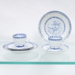 Dois(02) trios para xícaras para café em porcelana chinesa de exportação. Apresentam a técnica translúcida de recortes preenchidos por vidrado transparente mimetizando grãos de arroz (rice grain porcelain). A ornamentação em azul e branco sob o vidrado exibe no centro dos pratos a figura um dragão de cinco garras circundando a pérola flamejante central, ladeado por motivos de nuvens e névoas. Os pires e o fundo interno das xícaras ostentam um vaso com crisântemo e folhagens estilizadas. A cercadura periférica de cada exemplar recebe frisos geométricos repetitivos com o padrão ruyi e gregas tradicionais na cor azul-cobalto. O reverso apresenta base circular esmaltada com marca de manufatura carimbada em pigmento azul contendo caracteres ideográficos dispostos sobre a especificação em língua inglesa "MADE IN CHINA". Medidas: Xícara: Alt.: x Comp.: x Larg.: cm; Prato: Diam.: cm; Pires: Diam.: cm.