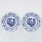 Porcelana Schmidt, Santa Catarina, Brasil (Fundada em 1945). Dois(02) pratos para pão / doce em porcelana nacional, esmaltagem vítrea na cor branca, borda contornadas por filete azul contínuo, Orla do pires circundada por cercadura perimetral ornamentada por ramagens relevadas na própria pasta. A ornamentação consiste em decalcomania monocromática sob o vidrado em tom azul-cobalto, reproduzindo o padrão clássico saxão Zwiebelmuster (padrão cebola), composta por uma faixa contínua de romãs, pêssegos, flores estilizadas e peônias ramificadas dispostas internamente e externamente, e na orla do pires. Padrão conhecido pelo senso comum como "cebolinha". Marcas da manufatura no verso. Medida: Diam.: 15,5 cm.