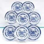 Conjunto de pratos em porcelana de pasta dura, produzido pela manufatura Renmin Cichang (Fábrica de Porcelana do Povo) em Jingdezhen, China, durante a segunda metade do século XX, circa 1969-1990. Esmaltagem vítrea na cor branca, apresentando aba perimetral recoberta por decorações transferidas sob o vidrado em tom azul-cobalto. A ornamentação exibe o célebre padrão "Blue Willow" de inspiração oriental Chinoiserie, guarnecido por cercaduras concêntricas em padrões de reticulados geométricos, pontilhados lineares e reservas com motivos fitomórficos abstratos instalados ao longo da borda. Centro abriga composição pictórica que reproduz uma gravação, retratando cenário paisagístico composto por pagode tradicionalizado de múltiplos tetos, pontes arqueadas com personagens, embarcações navegando ao fundo, salgueiro árvores frutíferas e o pássaros em revoada na porção superior central. Verso exibe base com anel de assentamento aparente e carimbo de manufatura transferido na cor azul, contendo as inscrições em caracteres chineses (Renmin Cichang) dispostos em arco sobre a localidade produtora (Jingdezhen). Composto de oito(08) unidades. Medida: Diam.: 18 cm.