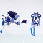 Duas(02 peças ornamentais em faiança, decoração em azul e branco à maneira de Delft, constituído por ornamento de suspensão modelado como anjo músico alado tocando trompa, corpo decorado com motivos florais em azul de cobalto, provido de argola metálica e fita azul; acompanha sineta ornamental de corpo campaniforme, rematada por laço, frutos e folhagem em relevo, com ornamentação floral no mesmo cromatismo. Peças destinadas à suspensão, associadas à tradição de ornamentos natalinos em Delft Blue. Medidas: Alt.: 6 x Comp.: 11 x Larg.: 2 cm; Alt.: 5,5 x Diam.: 4 cm.