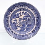 John Meir & Son, Tunstall - Inglaterra(Fundada em 1837, ativa até 1897). Prato de coleção em faiança inglesa do século XIX, fabricação inglesa datável do período vitoriano, circa 1855-1880. Decorado em "transfer printing" em azul sob vidrado. Medalhão central com composição do repertório "Blue Willow", reunindo pavilhões, ponte, embarcação, salgueiro, árvores, formações rochosas e par de aves em voo. Caveto preenchido por faixa reticulada geométrica; aba compartimentada por reservas com elementos arquitetônicos, motivos florais e objetos estilizados, delimitada por frisos geométricos. Marca da manufatura no verso. Apresenta craquelado caracterísito do material acentuado pela ação do tempo. Medida: Diam.: 20 cm.